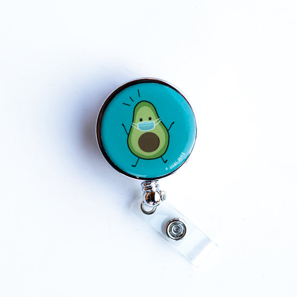 Lilac and Friends dental badge reel with avocado wearing a medical facemask on a turquoise background. The masked avocado dental badge reel for dental professionals by Lilac Paper.