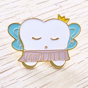 Enamel pin for Dental professionals with a tooth wearing a pink tutu, gold crown, and blue wings. Designed by Lilac Paper.