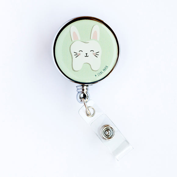Lilac and Friends dental badge reel with tooth dressed as a bunny on a light green background. Tooth Bunny dental badge reel for dental professionals by Lilac Paper.